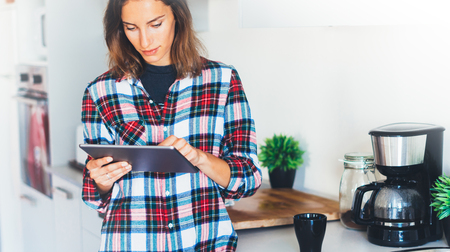 Hipster girl using tablet technology and drink coffee in kitchen, girl person holding computer on background interior cuisine, female hands texting message on relax holiday, templates gadget, blur lifestyleの写真素材