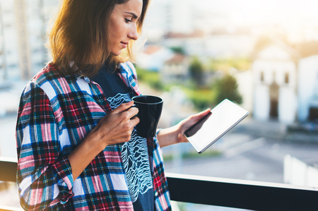 Hipster girl using tablet technology and drink coffee, girl person holding computer on background sun city, female hands texting message on relax holiday, mockup templates gadget, blur lifestyle travelの写真素材