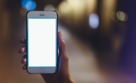hipster using in hands clean gadget mobile phone closeup, woman pointing finger on blank screen smartphone on background bokeh light in night atmospheric city, mockup street, online wifi internet conceptの写真素材