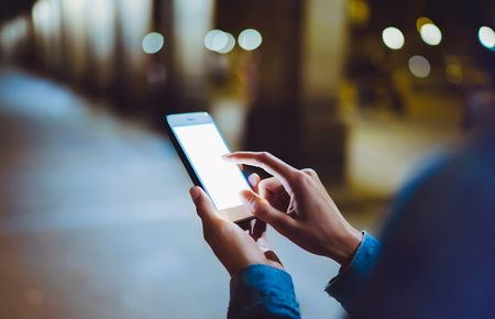 Woman pointing finger on blank screen smartphone on background bokeh light in night atmospheric city, hipster using in hands clean gadget mobile phone closeup, mockup street, online wifi internet conceptの写真素材