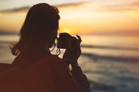 Hipster hiker tourist with backpack taking photo of amazing seascape sunset on camera on background blue sea, photographer enjoying ocean horizon, blurred panoramic sunrise blank mockup, traveler relax holiday concept, sunlight view in trip vacation northern spain の写真素材