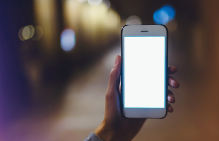 hipster using in hands clean gadget mobile phone closeup, woman pointing finger on blank screen smartphone on background bokeh light in night atmospheric city, mockup street, online wifi internet conceptの写真素材