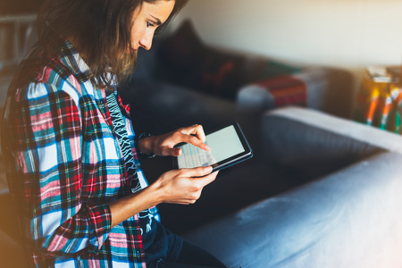 Hipster girl using tablet technology in home atmosphere, girl person holding computer with blank screen on background bokeh, female hands texting message on relax holiday, mockup templates gadget, blur lifestyle communication conceptの写真素材