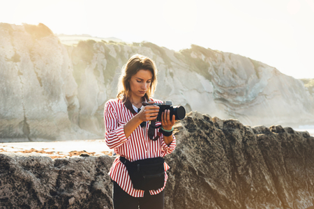 Hipster hiker tourist with backpack taking photo of amazing seascape sunset on camera on background mountains, photographer enjoying ocean horizon, blurred panoramic sunrise blank mockup, traveler relax holiday concept, sunlight view in trip vacation northern spain の写真素材