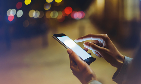 Woman pointing finger on blank screen smartphone on background bokeh light in night atmospheric...