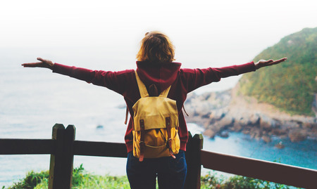 tourist traveler with backpack standing with raised hands, hiker looking to a valley in trip in spain, hipster young girl enjoying peak of mountain background seascape ocean horizon, relax holiday conceptの写真素材