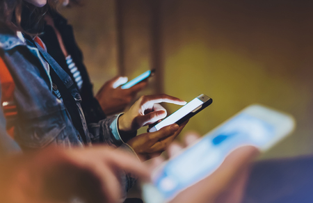 Group adult hipsters friends using in hands mobile phone closeup, street online wifi internet concept, bloggers together pointing finger on screen smartphone on background bokeh light in night atmospheric cityの写真素材