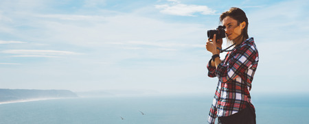 Tourist traveler photographer making pictures sea scape on photo camera on background ocean, hipster girl looking on nature horizon, relax holiday, blank space blue waves view, blurred backdrop for textの写真素材