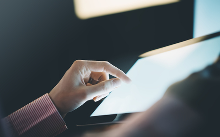 Ð¡loseup of a man pointing to a computer monitor with a blank screen blue against a background of bokeh light in the office horizontalの写真素材