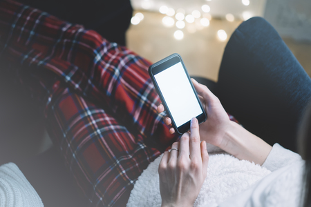 Closeup of a man using a black smartphone with a blank screen in the cozy atmosphere of Domani sitting in a chair against a background of bokeh lightの写真素材