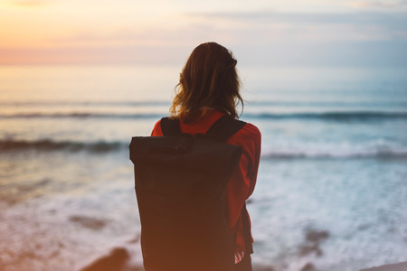 Hipster hiker tourist with backpack looking of amazing seascape sunset on background blue sea, photographer enjoying ocean horizon, blurred panoramic sunrise blank mockup, traveler relax holiday concept, sunlight view in trip vacation northern spain の写真素材