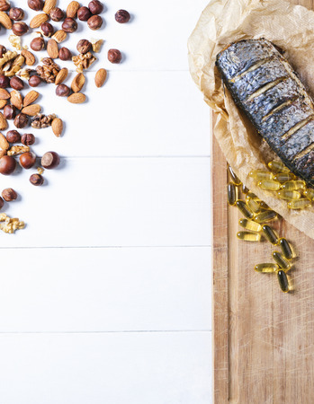 Baked fish with nuts and fish oil capsules on parchment paper and cutting board  on a white background of the old wooden boards vintage top view verticalの写真素材
