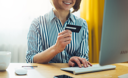 Hipster holding in hands credit card, women shopping online purchase, enjoy to buy internet, working at office with monitor computer, freelance manager typing message on keyboard, work process concept in workspace 
の写真素材