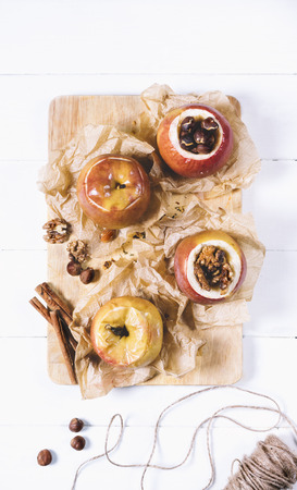 Baked apples with cinnamon sticks and hazelnuts on parchment paper on cutting board  on a white background of the old wooden boards vintage top view verticalの写真素材
