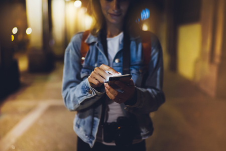 Woman pointing finger on blank screen smartphone on background bokeh light in night atmospheric city, blogger hipster using in hands gadget mobile phone closeup, mockup street, online wifi internet conceptの写真素材