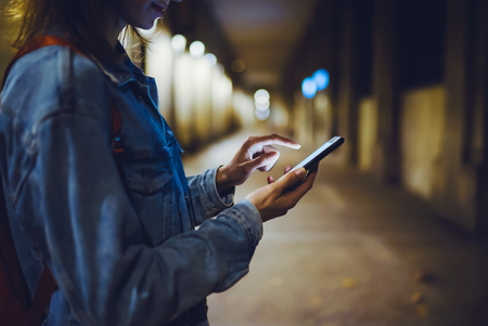 Woman pointing finger on blank screen smartphone on background bokeh light in night atmospheric city, hipster blogger using in hands clean gadget mobile phone, mockup street, online wifi internet conceptの写真素材