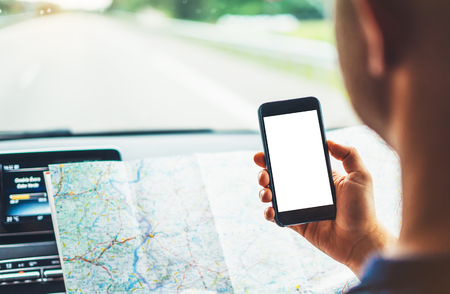 Hipster man looking on navigation map in car, tourist traveler driving and holding in male hands smartphone gps with clean screen display, panoramic view way road, trip in transportation from window autoの写真素材