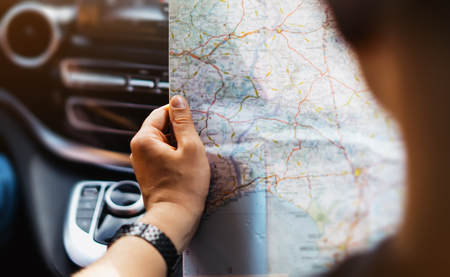 Hipster man holding in male hands and looking on navigation map in auto, tourist traveler hiker driving on background panoramic view way road, trip in transportation, person sitting on backdrop window autoの写真素材