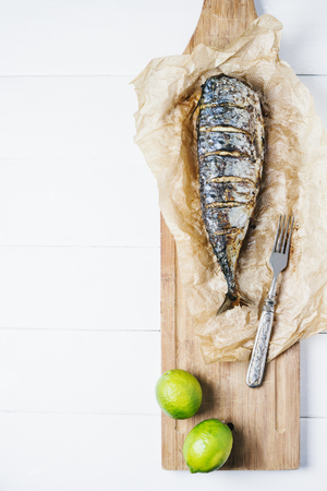 Baked fish with lime on parchment paper and cutting board on a white background of the old wooden boards vintage top view verticalの写真素材