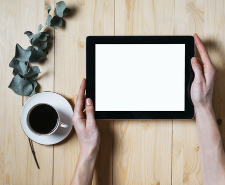 Closeup tablet with a empty blank screen monitor in the girls hands with a branch of eucalyptus and a cup of coffee on table background with natural wood planks wooden texture top view horizontal, digital computer with blank template copy space screenの写真素材
