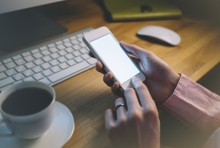 Girl using a smartphone with a clean blank screen display in business office atmosphere on the keyboard and cup of coffee on the wooden table backgroundの写真素材