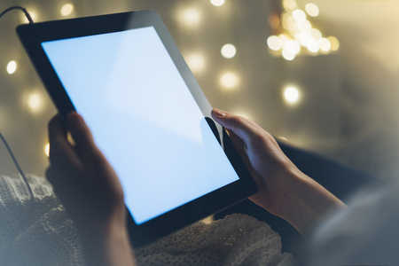 Girl using a tablet with a clean blank screen display in home atmosphere on the bokeh illuminated background, digital gadget in female hands in the night relax romantic atmosphereの写真素材