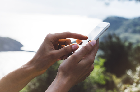 Hipster girl texting message on smartphone mobile close up, view tourist hands using gadget phone on device travel on background green mountains landscape; finger touch screen cellphone mockup natureの写真素材