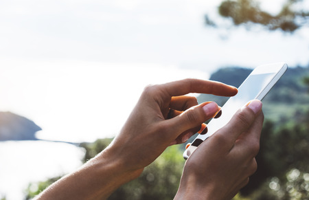 Hipster girl texting message on smartphone mobile close up, view tourist hands using gadget phone on device travel on background green mountains and blue sky landscape; finger touch screen cellphone mockup natureの写真素材