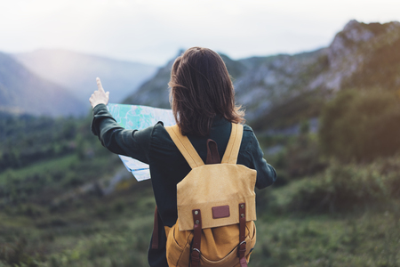 Hipster young girl with backpack enjoying sunset on peak of foggy mountain, looking a map and pointing hand.の写真素材