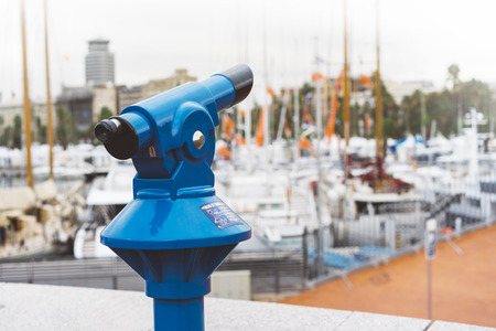 Touristic telescope look at the city with view of Barcelona Spain, close up old blue binoculars on background viewpoint  the pier port yacht, coin operated  in panorama observation nature, mockupの写真素材