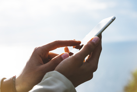 Hipster girl texting message on smartphone mobile close up, view tourist hands using gadget phone on device travel on background green mountains landscape; finger touch screen cellphone mockup natureの写真素材