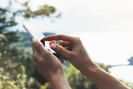 Hipster girl texting message on smartphone mobile close up, view tourist hands using gadget phone on device travel on background green mountains and blue sky landscape; finger touch screen cellphone mockup natureの写真素材