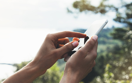 Hipster girl texting message on smartphone mobile close up, view tourist hands using gadget phone on device travel on background green mountains and blue sky landscape; finger touch screen cellphone mockup natureの写真素材