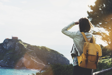 Hipster young girl with backpack enjoying sunset on seascape on peak mountain.の写真素材