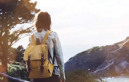 Hipster young girl with backpack enjoying sunset on seascape on peak mountain.の写真素材