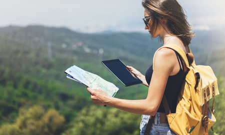 Hipster young girl with backpack enjoying panoramic mountain sea, using map and looking at horizon.の写真素材