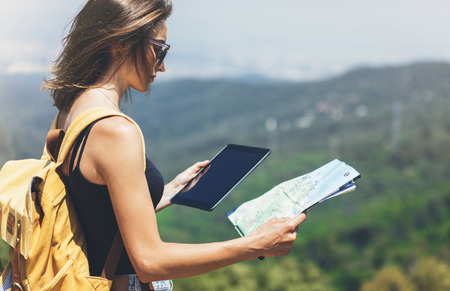Hipster young girl with backpack enjoying panoramic mountain sea, using map and looking at horizon.の写真素材