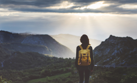 Hipster young girl with bright backpack enjoying sunset on peak of foggy mountain.の写真素材