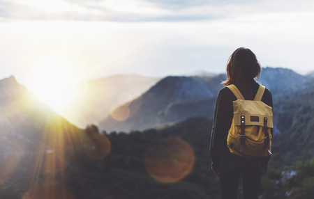Hipster young girl with bright backpack enjoying sunset on peak of foggy mountain.の写真素材