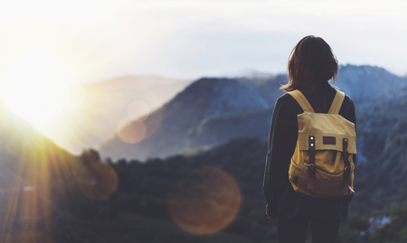 Hipster young girl with bright backpack enjoying sunset on peak of foggy mountain.の写真素材