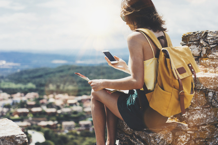 Hipster young girl with bright backpack looking at phone and map.の写真素材