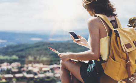 Hipster young girl with bright backpack looking at phone and map.の写真素材