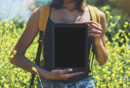Girl traveler using gadget on sun flare and yellow flowers background close. Female photographer take view on cell cameraの写真素材