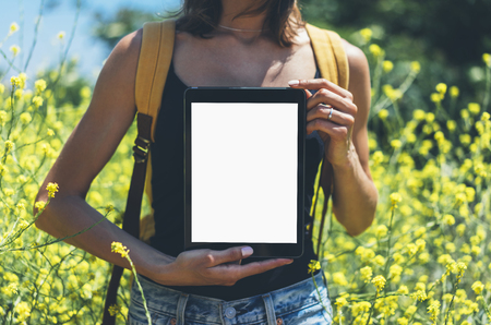 Girl traveler using gadget on sun flare and yellow flowers background close. Female photographer take view on cell cameraの写真素材