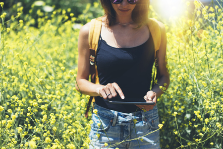 Girl traveler using gadget on sun flare and yellow flowers background close. Female hands photographer take view on cell cameraの写真素材