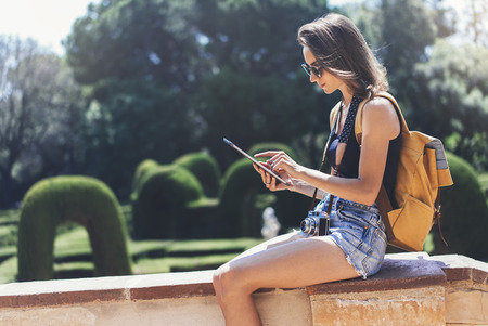 Hipster young girl with bright backpack and vintage camera using tablet or holding gadget, planning travel plan.の写真素材
