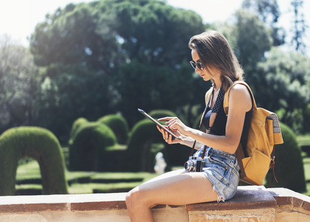 Hipster girl with backpack, sunglasses and vintage photo camera using tablet computerの写真素材
