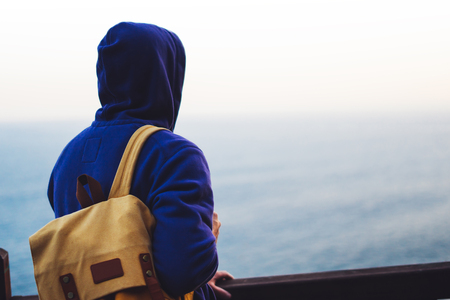 Hipster hiker tourist with backpack looking of amazing seascape sunset on background blue sea, guy...
