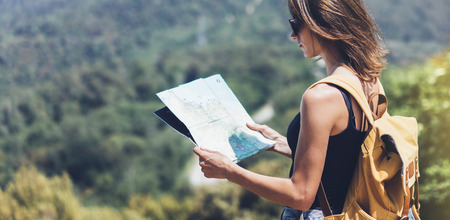 Hipster young girl with bright backpack enjoying panoramic mountain sea, using map and looking distance. Tourist traveler on background landscape Barcelona view mockup, sun flare in trip holidayの写真素材