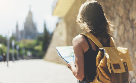 Hipster young girl with backpack using and looking at map. Said view tourist traveler enjoying on background panoramic city. Person visiting the sights Barcelona in holiday. Mockup for text messageの写真素材